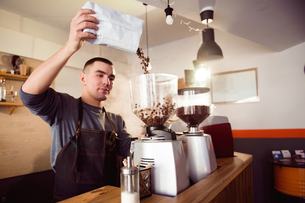 Barista fait du café au café. Barista moudre les haricots avec une machine à café. Moulin à café broyant les grains torréfiés en poudre.