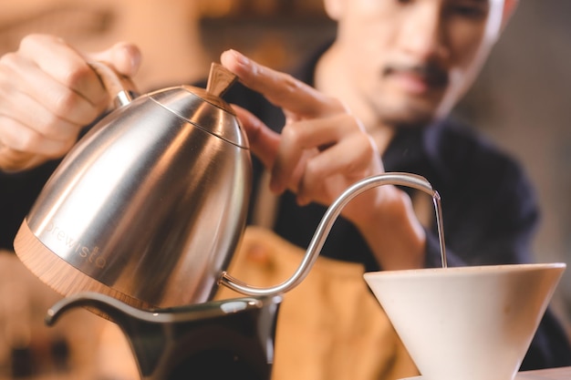 Barista hipster versant de l'eau chaude pour faire du café avec un style goutte à goutte ou filtre dans un café infusion lente pour une boisson aromatisée à la caféine dans une tasse de café noir frais et d'espresso pour le petit déjeuner