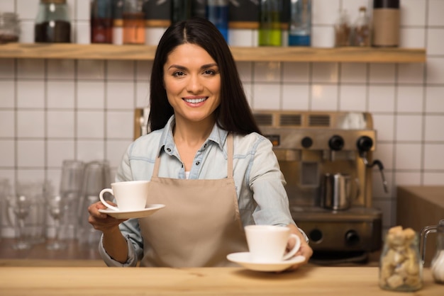 Barista joyeux tenant deux tasses de café et regardant la caméra