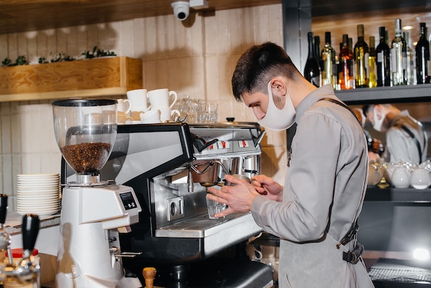 Un barista masqué prépare un délicieux café au bar d'un café. Le travail des restaurants et cafés pendant la pandémie.