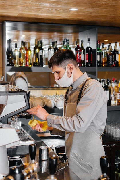Un barista masqué prépare un délicieux café au bar d'un café. Le travail des restaurants et cafés pendant la pandémie.