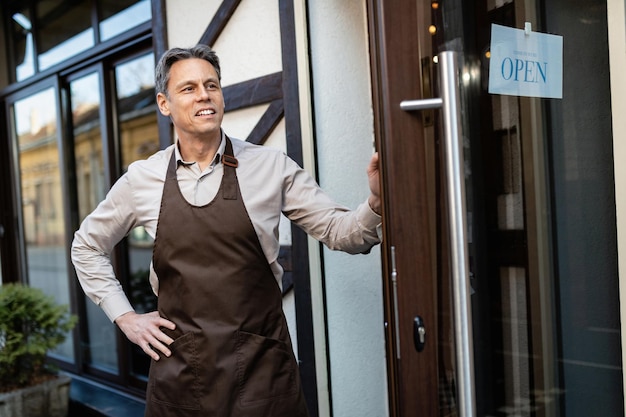 Barista mi-adulte attendant un invité debout à la porte d'entrée du bar