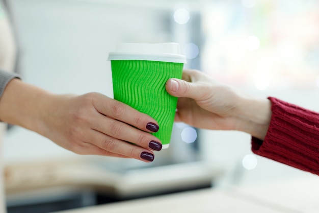 Barista offre au client du café chaud dans une tasse de papier à emporter verte. Café à emporter au café