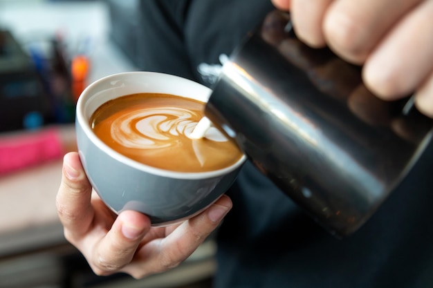 Photo barista préparant un café latte versant du lait dans un gros plan de café sur des mains masculines avec de l'art latte