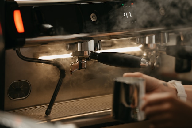 Un barista prépare à purger une tasse en métal avec de la vapeur dans une machine à expresso professionnelle