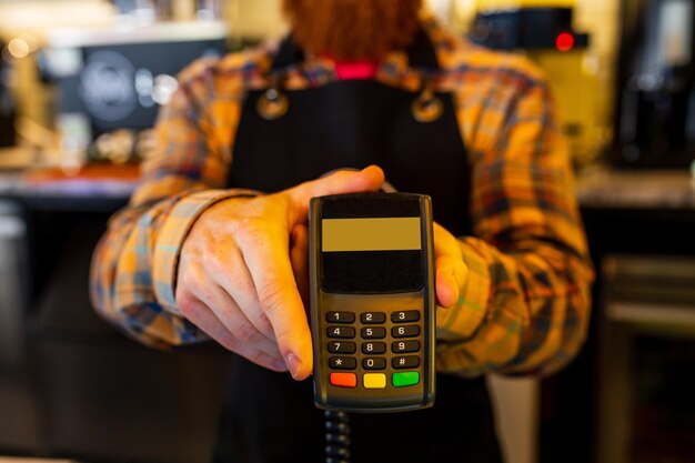 Barista professionnel jeune homme barbu au gingembre roux en tablier noir travaillant dans un café