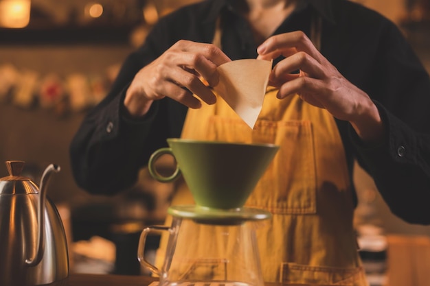 Barista professionnel préparant une boisson chaude sur une tasse de café au café-bar préparant une boisson chaude à la caféine et fabriquant à partir d'une machine lente avec un petit-déjeuner filtre sur fond de style vintage marron et noir