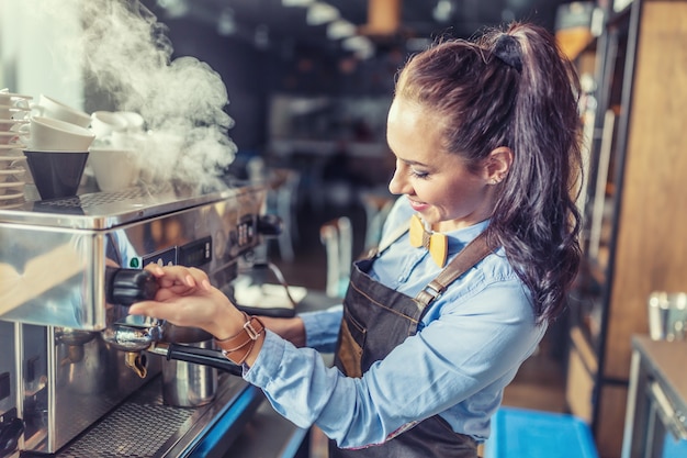 Une barista professionnelle et bien habillée fume une machine à café dans un café.