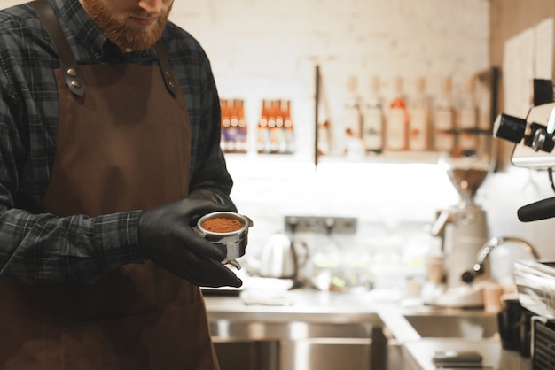 Barista se tient dans un café avec un support avec du café dans les mains.