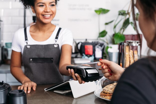 Photo barista souriant dans le tablier tenant le terminal pos tandis que le client paie par carte