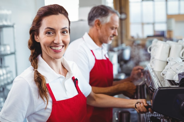 Barista souriant en utilisant la machine à café avec un collègue derrière