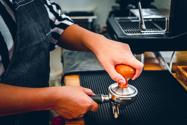 Barista tenant un porte-filtre et un bourreur de café faisant un café expresso au café