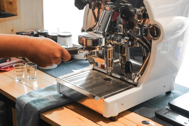 Barista tenant un porte-filtre à café avec du café moulu près d'une machine à expresso professionnelle