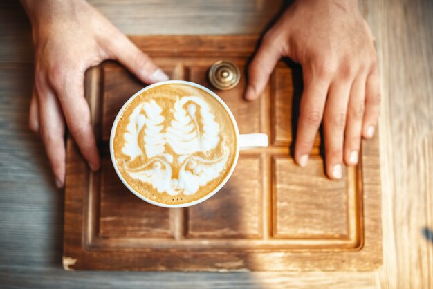 Barista tient une tasse de café avec un dessin en mousse