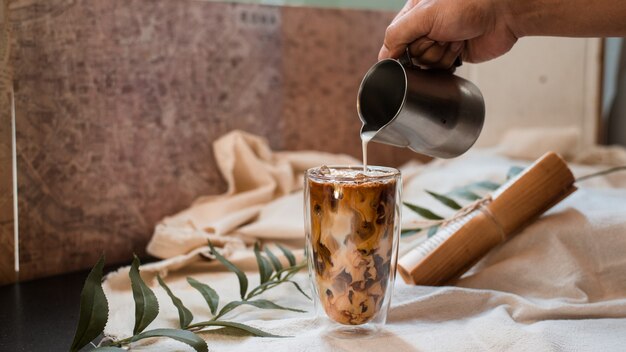 Barista versant du lait dans un verre de café glacé