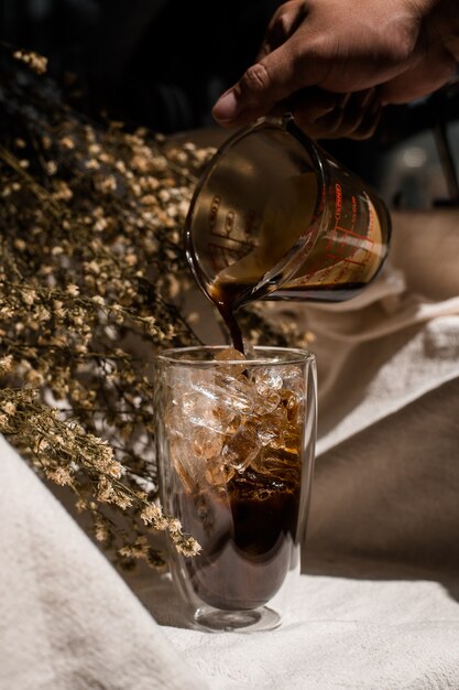 Barista versant du lait dans un verre de café glacé