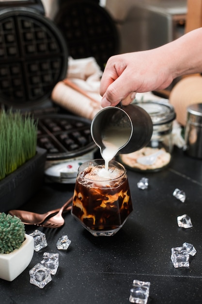 Barista versant du lait dans un verre de café glacé