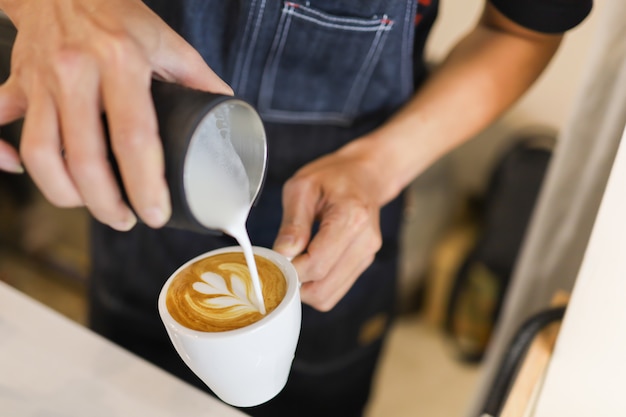 Barista versant du lait mélangé dans une tasse blanche de café chaud pour créer un art au latte.