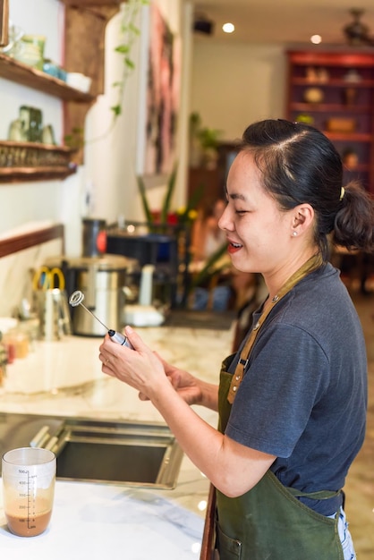 Barista vietnamien tenant un mélangeur pour le lait condensé dans une tasse en verre pour préparer le café vietnamien C