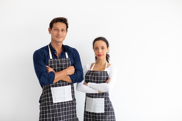 Baristas hispaniques homme et femme portant des bras de tablier noir croisés sur fond blanc.