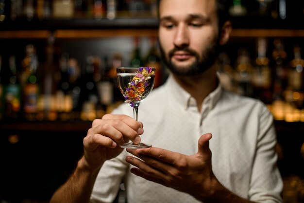 Barman attrayant présentant un cocktail dans le verre décoré de fleurs