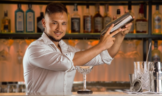Photo barman avec un charmant sourire prépare une délicieuse boisson en secouant