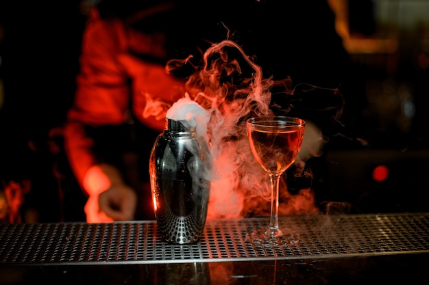 Barman debout au premier plan d'un cocktail dans le shaker en verre et acier fumé