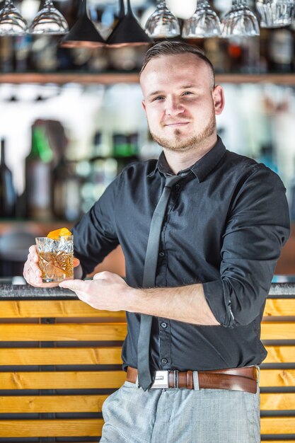 Barman debout devant le bar et dans la main tenant un cocktail.