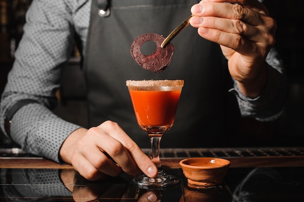 Barman décorer un verre à cocktail rempli d'une boisson alcoolisée rouge avec du sel et de la betterave