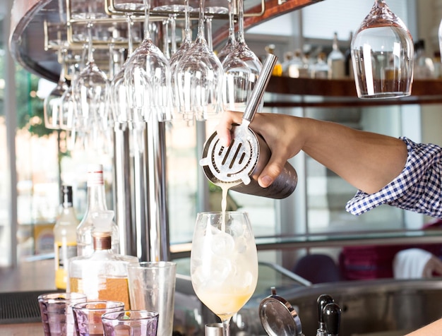 Photo le barman derrière le comptoir du bar tient un shaker en acier et verse une boisson mélangée dans le verre avec un cocktail.