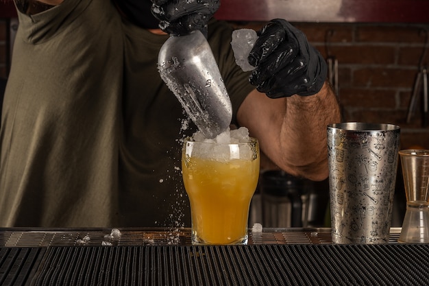 Le barman du bar verse de la glace dans un cocktail alcoolisé orange