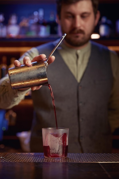 Photo un barman élégant et sérieux versant du sirop d'une tasse de mélange dans un verre.