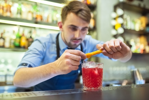 Le barman fait un cocktail rouge avec une orange sur le bar