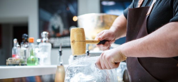 Barman de glace pilée manuellement avec un marteau en bois et un couteau en métal.