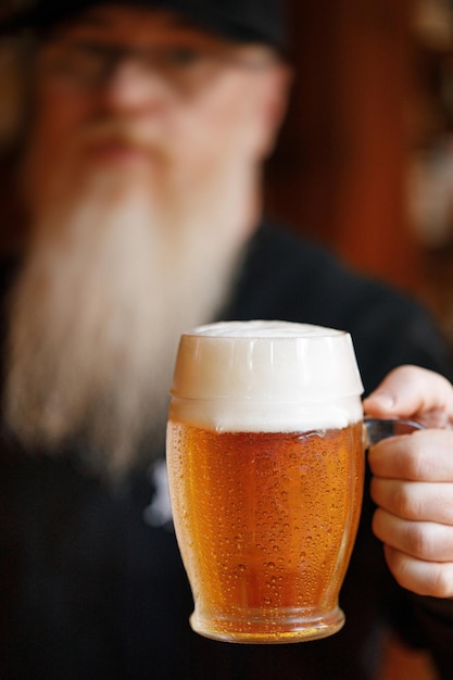 Un barman avec une grande barbe blanche tient une chope de bière