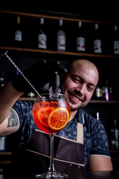 Barman mettant au verre de cocktail de seringue Aperol frais et savoureux paix de glace