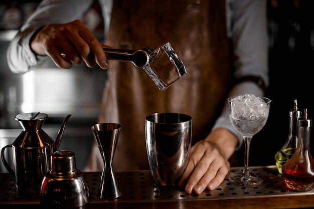 Barman mettant un gros cube de glace avec des pincettes dans le shaker en acier