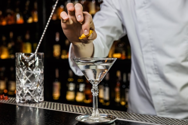 Barman préparant un cocktail au bar, en serrant un zeste de citron sur une boisson dans un verre à martini