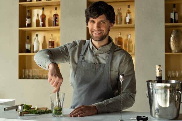 Le barman prépare un mojito cocktail en utilisant le barman madler écrase la menthe et le citron vert avec un madler