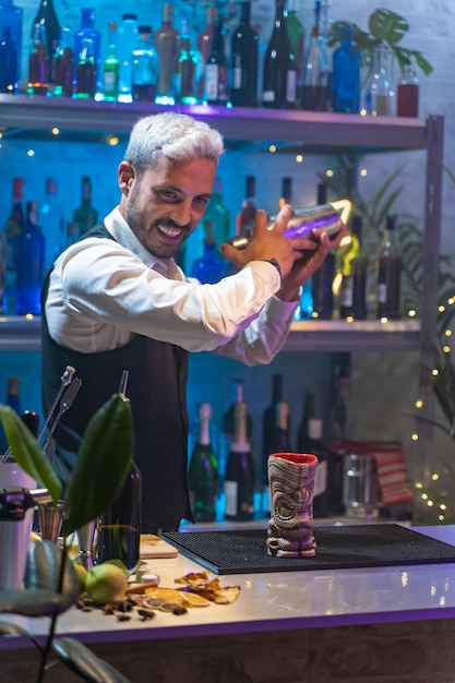 Un barman professionnel en chemise blanche et tablier noir tient un shaker en acier dans ses mains