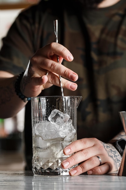 Un barman professionnel remue un cocktail froid avec une cuillère Plusieurs bouteilles de boissons alcoolisées et des verres debout sur le comptoir du bar