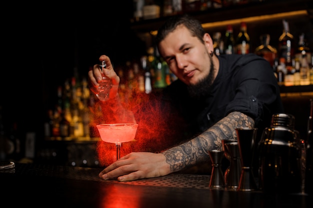 Barman professionnel saupoudrant d'amer de couleur rouge dans un verre à cocktail