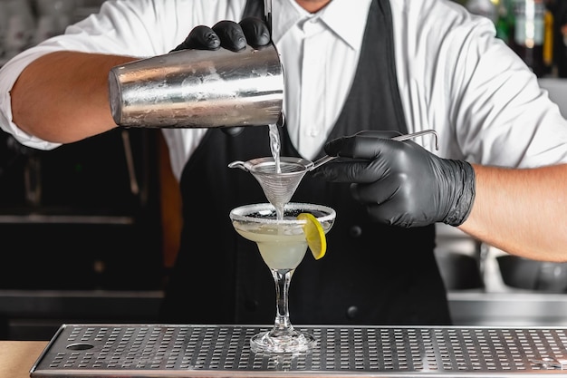 Photo barman professionnel avec un shaker dans ses mains faisant un cocktail alcoolisé margarita.