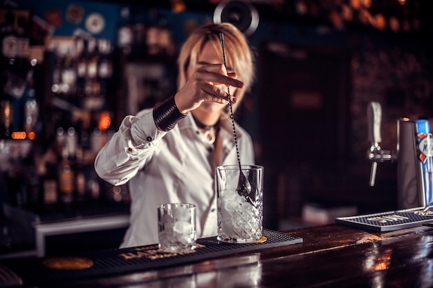 Une barman professionnelle termine intensément sa création tout en se tenant près du comptoir du bar dans la discothèque