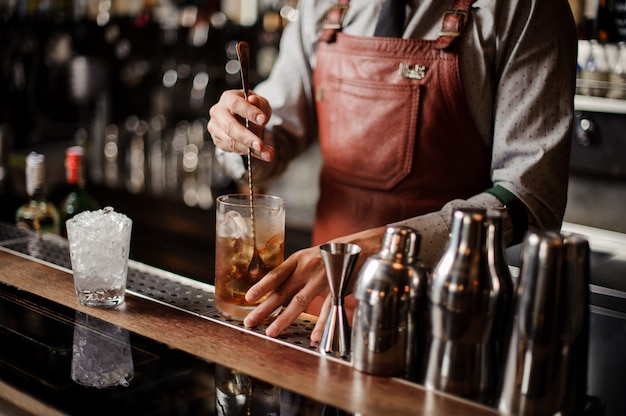 Le barman refroidit un verre de cocktail en mélangeant de la glace avec une cuillère.