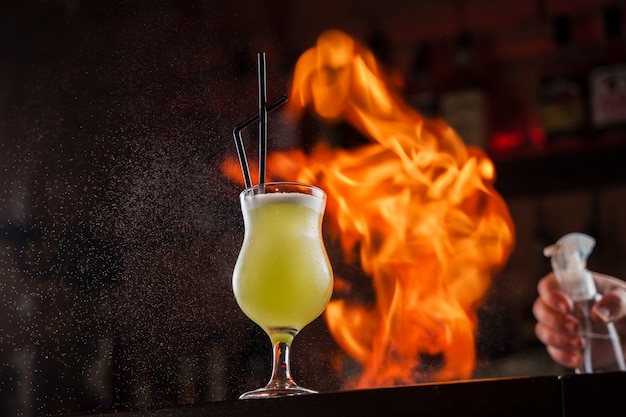 Le barman saupoudre sur le verre illuminé d'un cocktail froid vert vif sur le comptoir du bar et fait flamber le feu dessus.