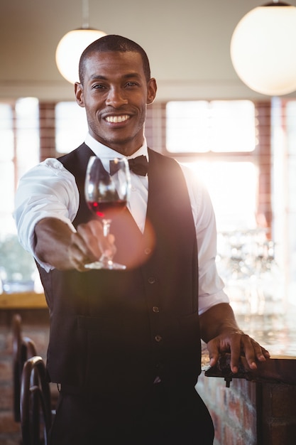 Barman souriant offrant un verre de vin au comptoir du bar