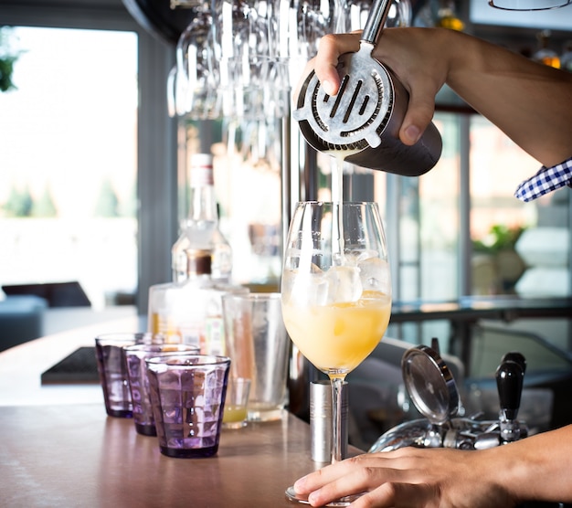 Barman tenant le shaker en acier et versant la boisson mélangée dans le verre avec un cocktail.