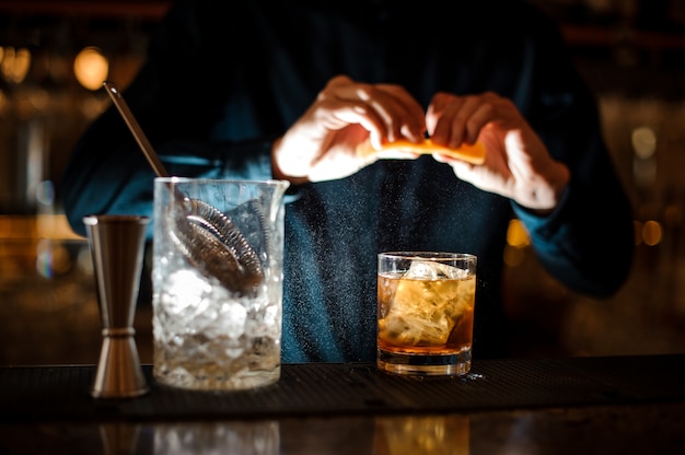 Barman termine la préparation d'un cocktail alcoolisé à l'ancienne en ajoutant une orange amère