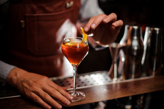 Barman avec verre et zeste de citron prépare un cocktail au bar